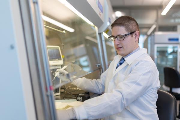 Crime Lab Employee, male wearing a white lab coat and goggles while testing blood sample for alcohol and drugs