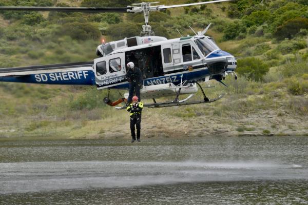 Helicopter hovering over a lake, body of water while rescuer is being hoisted down to rescue someone.